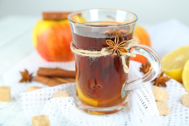 Boisson chaude dans une tasse en verre avec des fruits et des épices, sur fond de bois