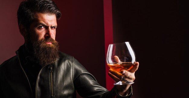 Boisson chère. Homme en veste de cuir buvant du cognac ou du cognac. Homme barbu avec un verre de whisky.