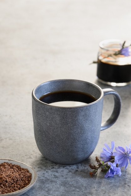 Boisson à la chicorée comme substitut de café dans une tasse grise et des fleurs fraîches. Format vertical.