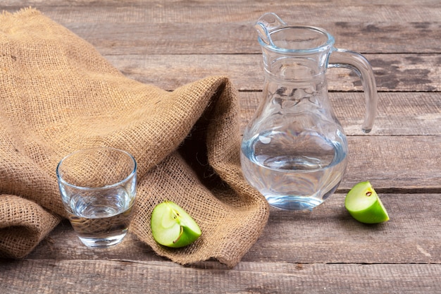 Boisson diététique de désintoxication avec des tranches de pomme dans de l'eau propre et une pomme fraîche sur une table en bois, gros plan