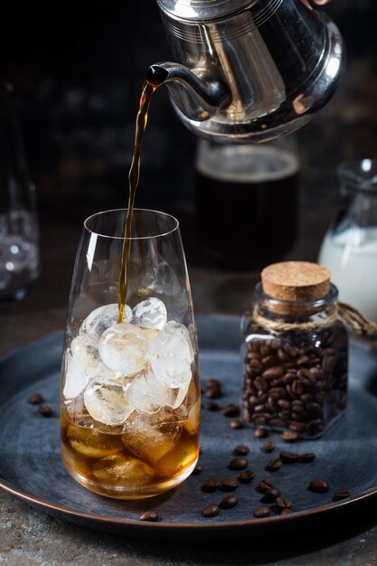 Boisson d'été froide au café glacé dans un grand verre avec du café et des grains de café sur fond de pierre.