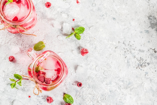 Boisson d'été froide, framboise sangria, limonade ou mojito avec framboise fraîche et sirop, feuilles de menthe, sur fond gris pierre vue de dessus