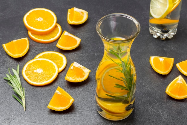 Boisson d'été infusée avec des bleuets oranges et du romarin en bouteille Tranches d'orange tranchées et brin de romarin sur table