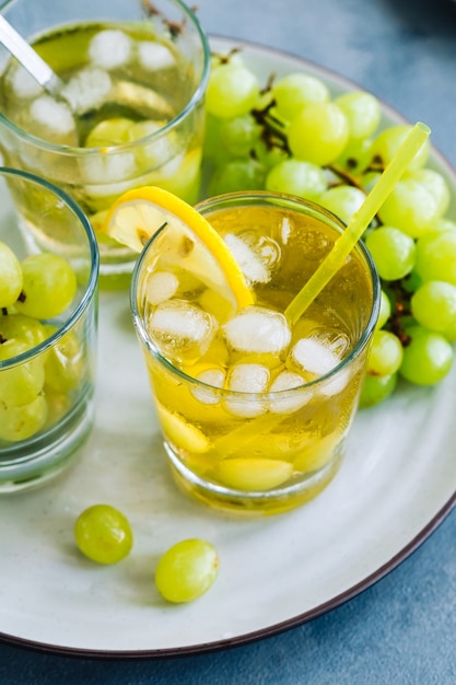 Boisson d'été rafraîchissante en verre avec glaçons, raisin vert et citron sur la table.