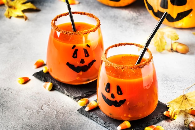 Photo boisson festive orange halloween et gardes de citrouille sur fond d'automne gris avec des feuilles tombées de maïs sucré et des feux de feu mise au point sélective