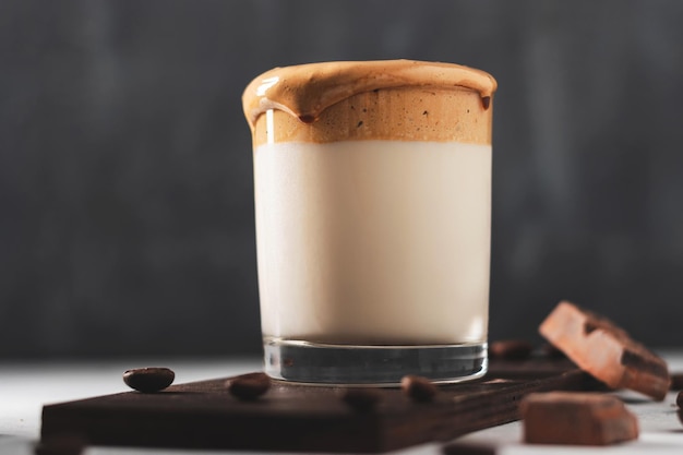 Boisson fouettée au café Dalgona dans un verre avec du lait, fond sombre.