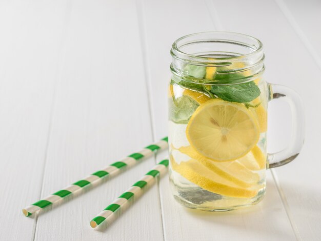 Boisson fraîche de citron, menthe et gingembre avec deux tubes à cocktail sur un tableau blanc