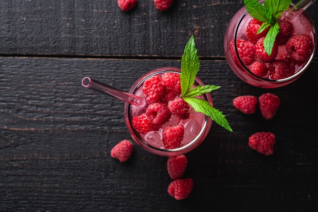 Boisson fraîche de jus de baies glacées à la menthe, limonade aux framboises d'été dans deux verres avec des pailles sur une table en bois foncé