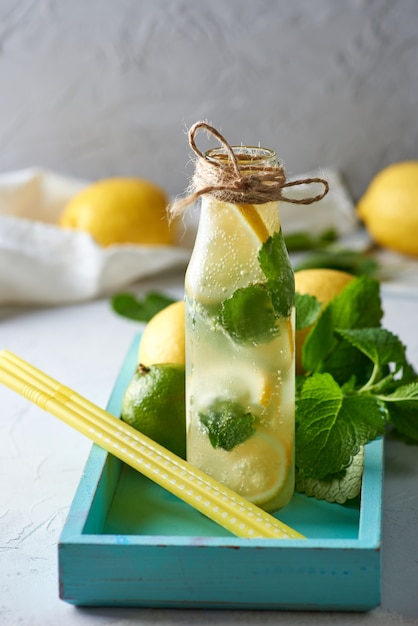 Boisson froide aux citrons, feuilles de menthe, citron vert dans une bouteille en verre