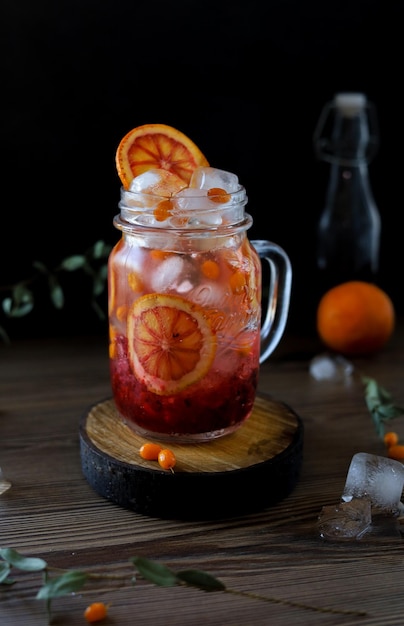 Boisson froide saine faite maison avec des baies d'argousier de saison, de l'orange et de la glace sur fond sombre