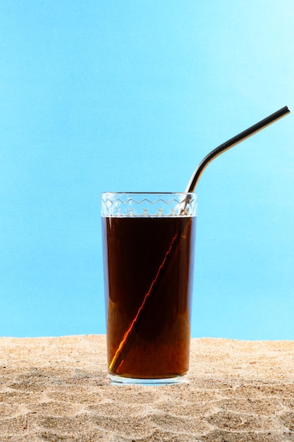 Boisson froide en verre avec de la paille métallique sur le sable sur fond bleu Gros plan