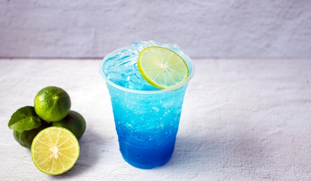 Boisson hawaïenne bleue dans un verre en plastique et citron vert sur fond blanc