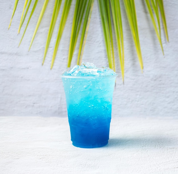 Boisson hawaïenne bleue dans un verre en plastique et des feuilles de noix de coco