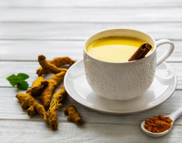 Boisson de latte au curcuma jaune. Lait doré avec cannelle, curcuma, gingembre et miel sur une surface en bois blanche.