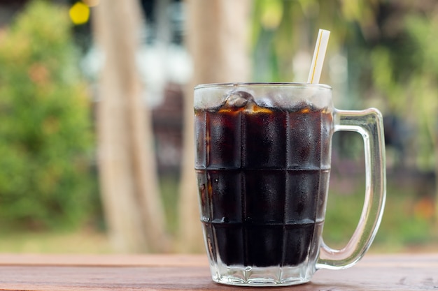 boisson non alcoolisée Cola glacé dans une vue de côté en verre sur le bureau en bois avec fond porte sur vert naturel pendant la journée en été