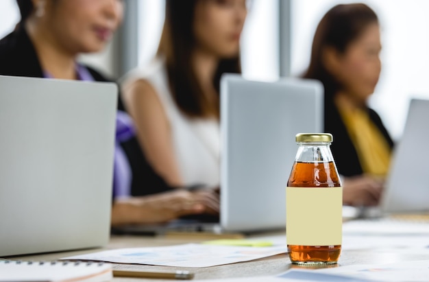 Boisson nutritive naturelle dans un produit en bouteille de verre servi à une femme d'affaires asiatique assoiffée à boire pour se rafraîchir la santé, se nourrir pendant le travail de bureau sur un ordinateur portable et un séminaire lors d'une conférence d'entreprise