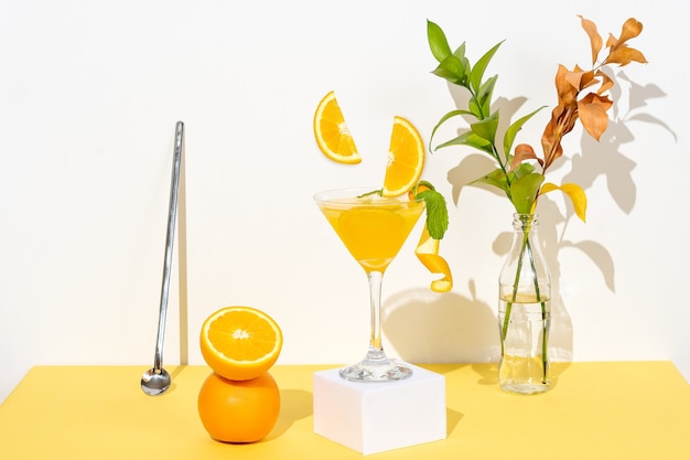 Boisson à l'orange sur une table avec sculpture jaune et fond blanc, oranges comme décoration