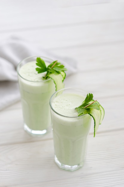 Boisson rafraîchissante au lait fermenté au concombre et aux herbes. Deux avec un tel cocktail dans un intérieur clair sur une table blanche.