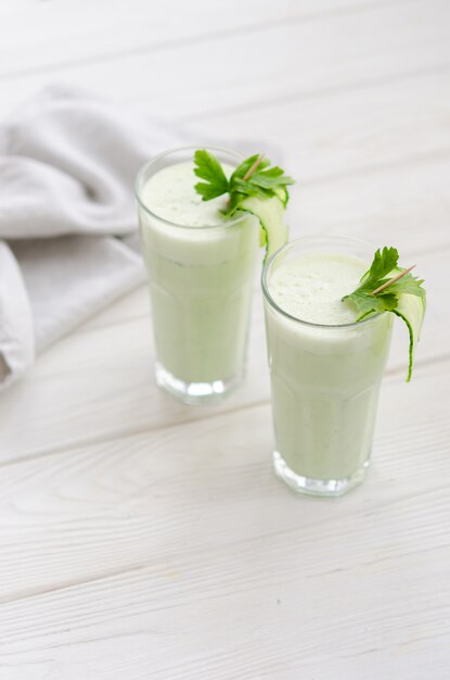 Boisson rafraîchissante au lait fermenté au concombre et aux herbes. Deux avec un tel cocktail dans un intérieur clair sur une table blanche.