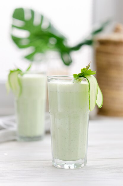 Boisson rafraîchissante au lait fermenté au concombre et aux herbes. Deux avec un tel cocktail dans un intérieur clair sur une table blanche.