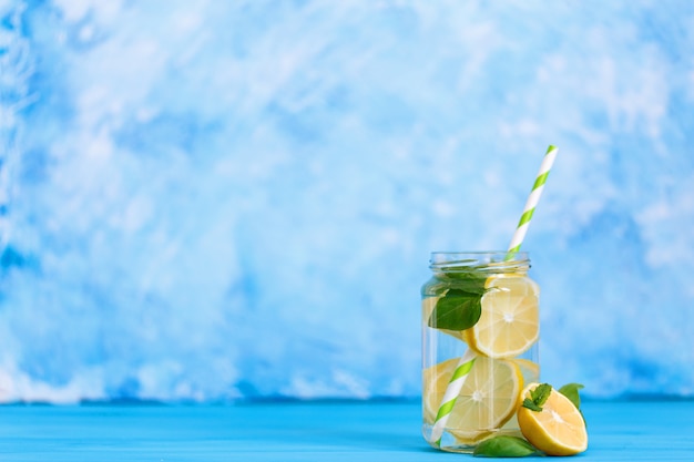 Boisson savoureuse au citron et basilic dans un bocal en verre sur fond bleu