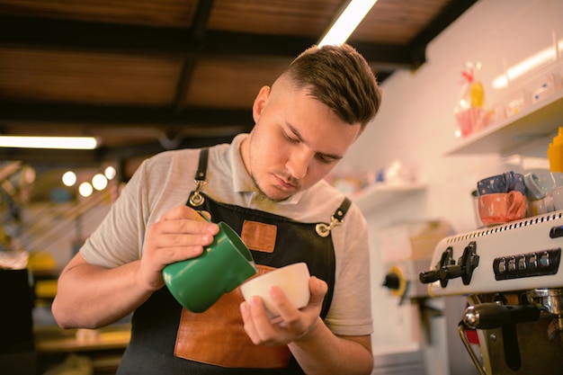 Boisson savoureuse. Jeune homme attentif s'inclinant la tête tout en faisant une photo sur latte