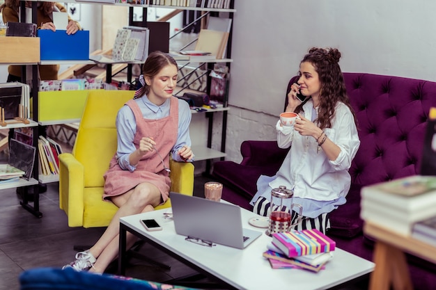 Boisson Sucrée Au Cacao. Belles Femmes à La Mode Assis Dans La Zone De Refroidissement De La Librairie Et Observant Des Informations Dans Un Ordinateur Portable