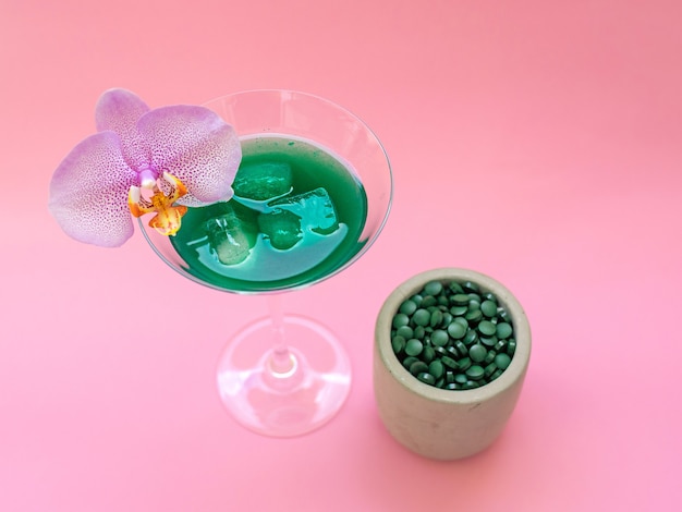 Boisson verte à la spiruline liquide avec Phalaenopsis en verre à cocktail et pilules de spiruline