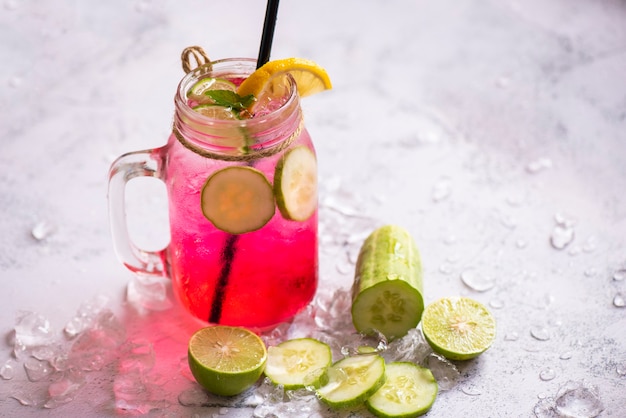 Boissons d'été exotiques rafraîchissantes de verres de boissons froides pot de fruits et légumes frais sur glace thé cocktail maison avec mojito citron vert et concombre, boisson d'été colorée rose rouge juteuse