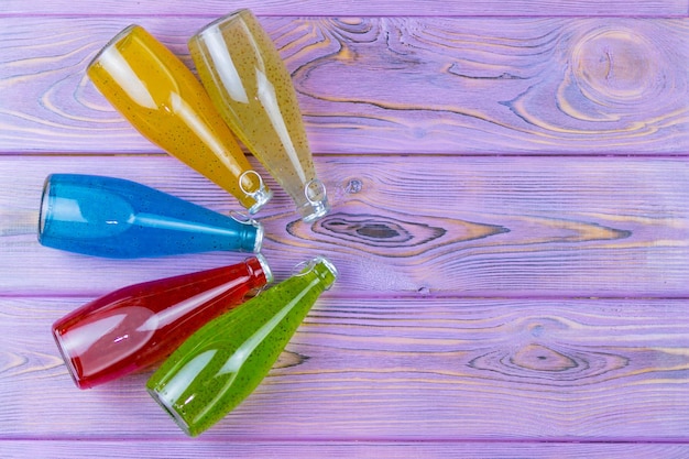 Boissons multicolores avec des graines en bouteilles sur un fond de bois violet