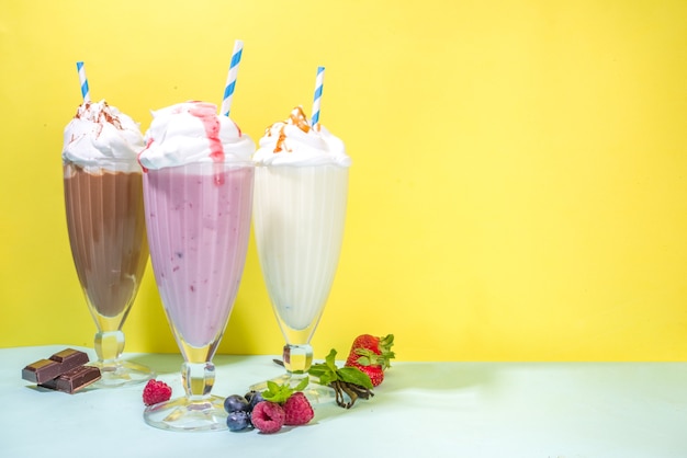 Boissons rafraîchissantes d'été, milkshakes, shakes fous avec crème glacée, baies, vanille, chocolat. Sur un fond jaune bleu clair