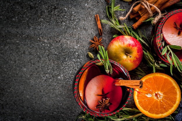 Boissons traditionnelles d'hiver et d'automne. Cocktails de Noël et de Thanksgiving. Vin chaud à l'orange, pomme, romarin, cannelle et épices sur une pierre sombre, vue du dessus