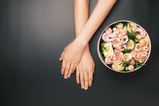 Boîte avec de belles fleurs à côté des mains de la femme sur le fond noir avec espace de copie. Beauté