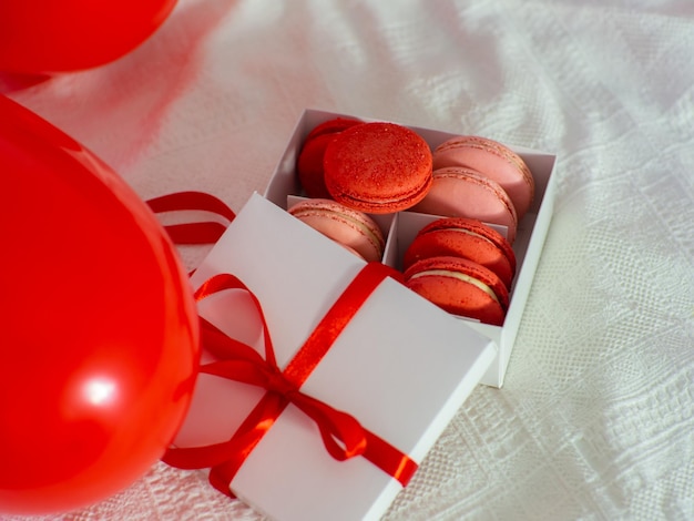 Boîte avec biscuits macaron et ballons rouges sur le lit