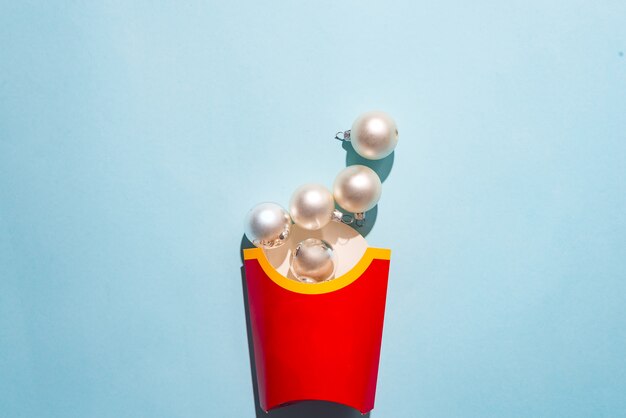 Photo boîte blanche de frites avec des boules blanches du nouvel an sur un fond de papier bleu,