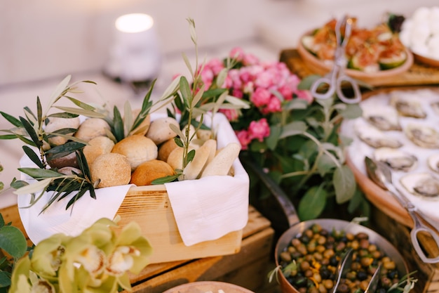 Boîte en bois avec des petits pains sur le fond des olives farcies aux huîtres et un bouquet de fleurs