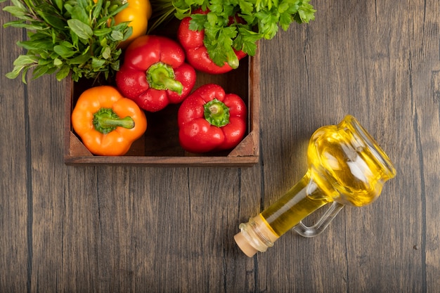 Boîte en bois de poivrons frais et d'huile d'olive sur une surface en bois