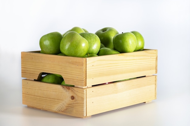 Boîte en bois de pommes vertes sur fond blanc.