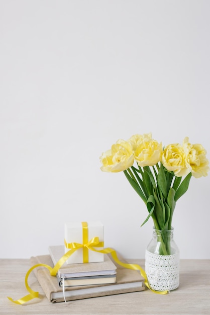 Une boîte-cadeau avec un arc sur le lieu de travail avec des bouquets de fleurs jaune vif et une pile de cahiers ou de livres. Fleurs pour une femme d'affaires. Un cadeau à un collègue.
