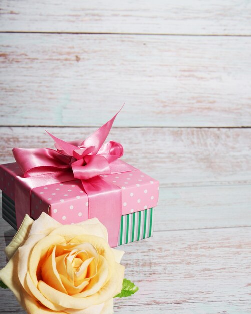 Une boîte-cadeau avec un arc rose sur un fond en bois, copie de l'espace texte une rose à proximité.