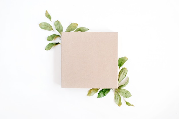 Boîte-cadeau artisanale et composition florale avec des feuilles vertes sur une surface blanche