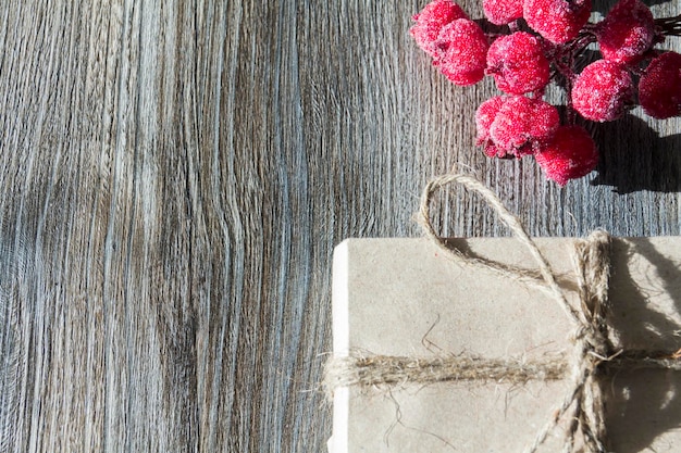 Une boîte-cadeau avec des baies rouges emballées dans du papier kraft et attachées avec de la ficelle de lin sur un fond en bois