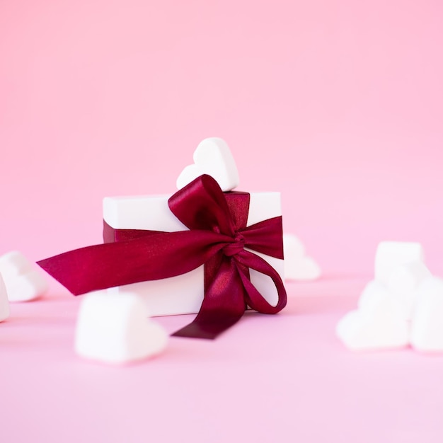 Boîte-cadeau blanche avec arc rouge sur fond rose avec des coeurs rouges Bannière de vacances Vue de dessus Happy Valentines Day