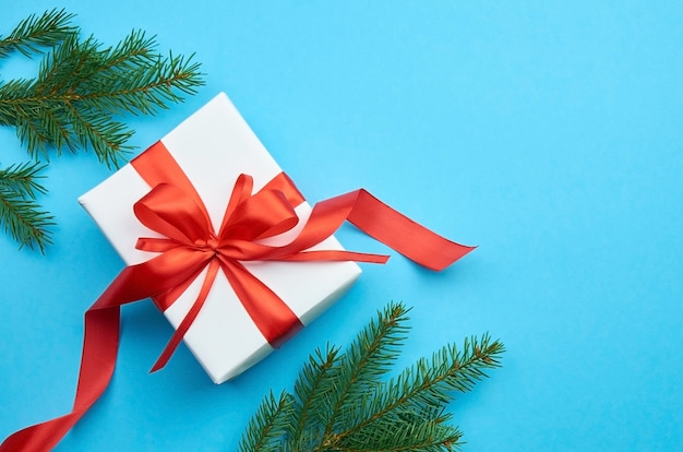 Boîte cadeau blanche avec noeud de ruban rouge avec des branches de pin