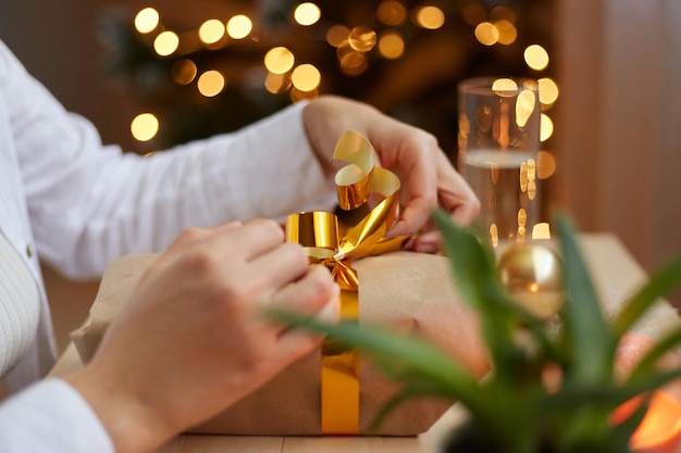 Boîte-cadeau d'emballage féminine méconnaissable Mains de femme avec cadeau de Noël dans les mains près de l'arbre de Noël personne anonyme préparant la boîte-cadeau pour les vacances du nouvel an