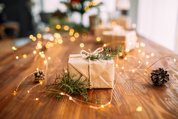 Boîte cadeau enveloppé de métier sur la table en bois avec guirlande et branches de sapin