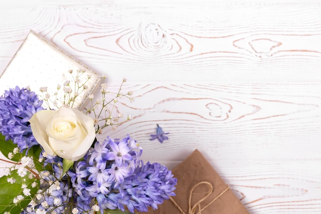 Une boîte cadeau enveloppée de papier et de fleurs de jacinthe bleu, roses blanches sur un plateau de table blanc