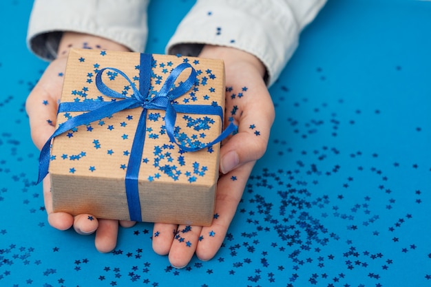 Boîte cadeau étincelante enveloppée dans du papier kraft et attachée avec un arc dans les mains de l'enfant