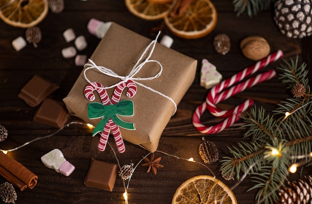 Boîte-cadeau avec des guimauves, des bonbons, de la cannelle, des cônes et du chocolat sur une table en bois marron, vue du dessus