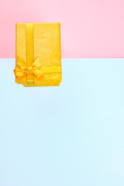 Boîte cadeau jaune avec ruban noeud sur fond rose et bleu, anniversaire